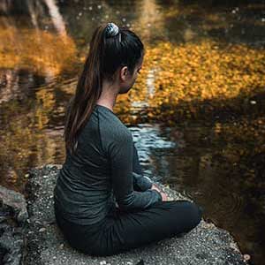 A girl sat peacefully near a body of water, embracing her natural surroundings 